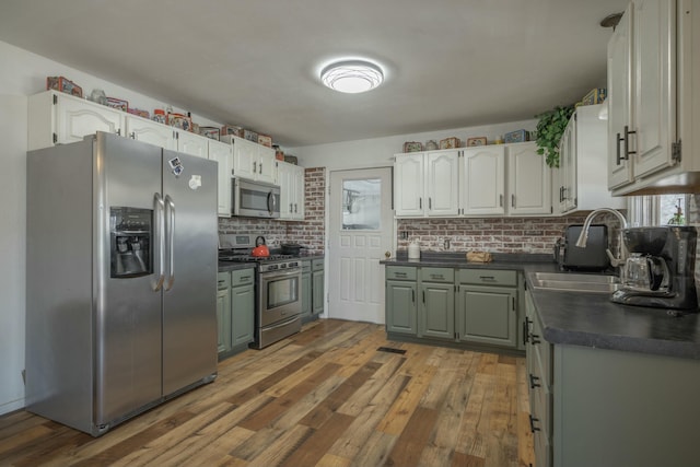 kitchen with dark countertops, decorative backsplash, wood finished floors, stainless steel appliances, and a sink