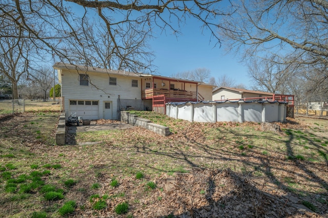 rear view of property featuring a covered pool, an attached garage, fence, and a wooden deck