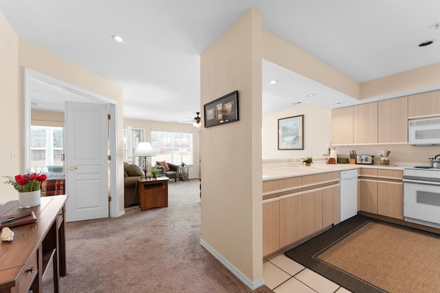 kitchen with light brown cabinets, light countertops, carpet floors, white appliances, and a ceiling fan