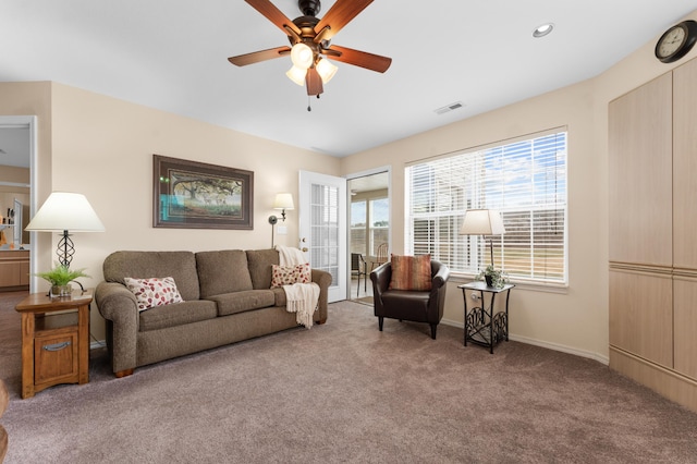 living area featuring visible vents, carpet floors, plenty of natural light, and a ceiling fan