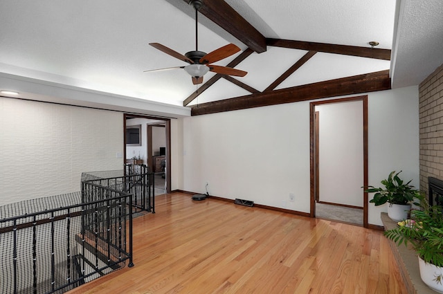 empty room featuring a ceiling fan, lofted ceiling with beams, light wood-style floors, and baseboards