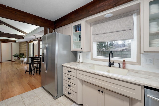 kitchen with light stone countertops, beam ceiling, a sink, white cabinets, and stainless steel fridge