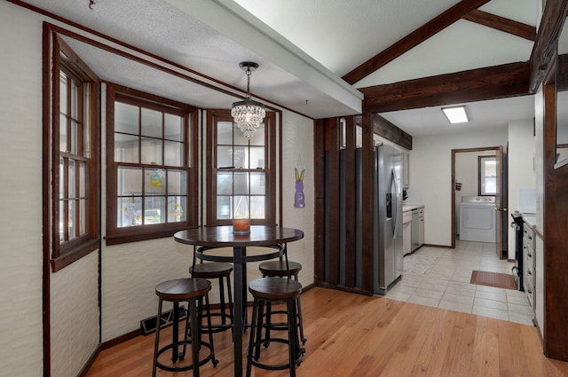 dining space with vaulted ceiling with beams, light wood-type flooring, an inviting chandelier, washer / clothes dryer, and a textured ceiling