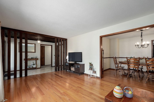 living room with baseboards, a notable chandelier, a textured ceiling, and light wood-style floors