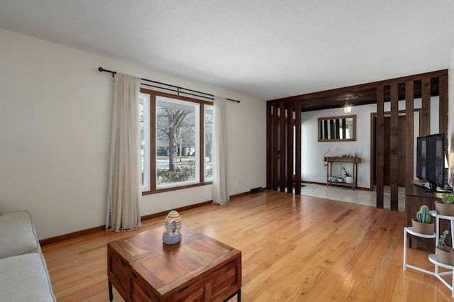 living area with light wood-type flooring, baseboards, and a textured ceiling