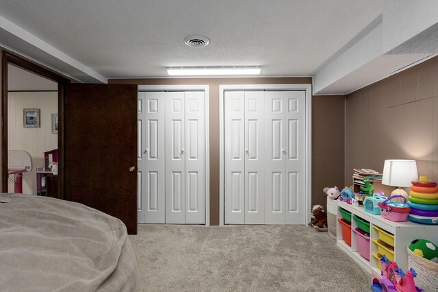 carpeted bedroom featuring visible vents, multiple closets, wood walls, and a textured ceiling