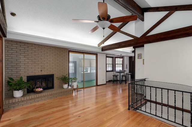 living room featuring a brick fireplace, ceiling fan, lofted ceiling with beams, wood finished floors, and a textured ceiling