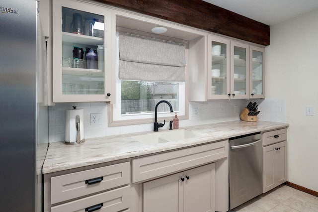 kitchen with a sink, glass insert cabinets, decorative backsplash, light stone countertops, and dishwasher