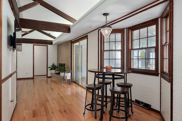 dining area with lofted ceiling with beams, light wood-style flooring, a notable chandelier, and visible vents