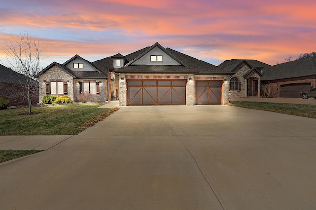 view of front of property featuring stone siding, a lawn, a garage, and driveway