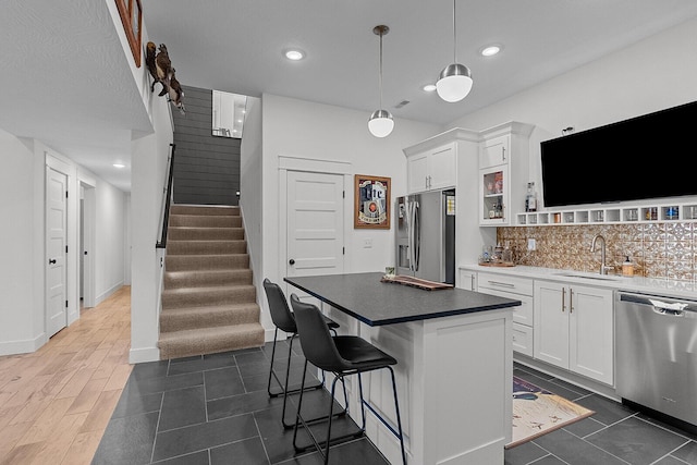 kitchen featuring a breakfast bar area, a sink, stainless steel appliances, white cabinetry, and backsplash