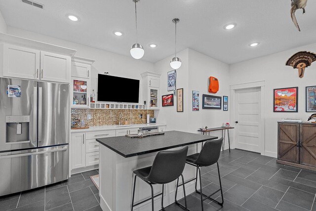 kitchen featuring a sink, white cabinets, stainless steel refrigerator with ice dispenser, a kitchen bar, and backsplash