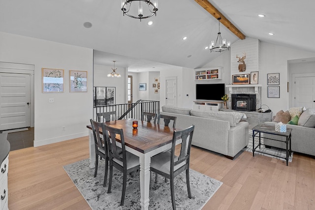 dining space featuring a notable chandelier, light wood finished floors, baseboards, vaulted ceiling with beams, and a tile fireplace