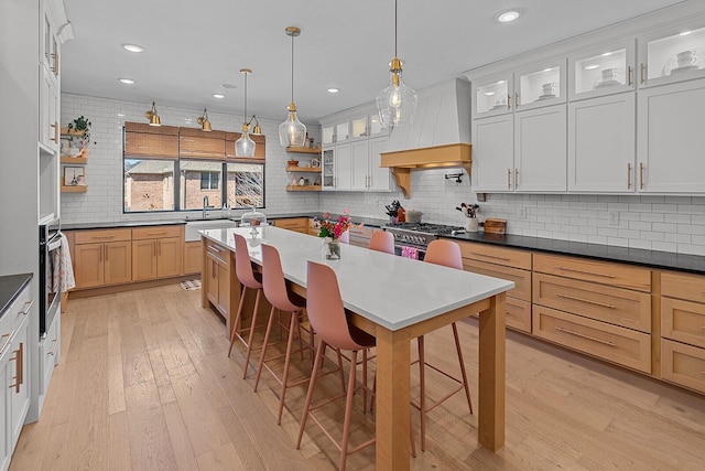 kitchen featuring a center island, a breakfast bar, custom range hood, stainless steel appliances, and open shelves