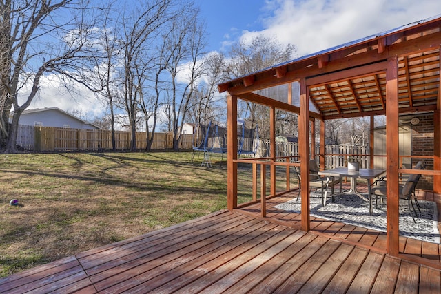 wooden deck featuring a trampoline, a fenced backyard, and a yard