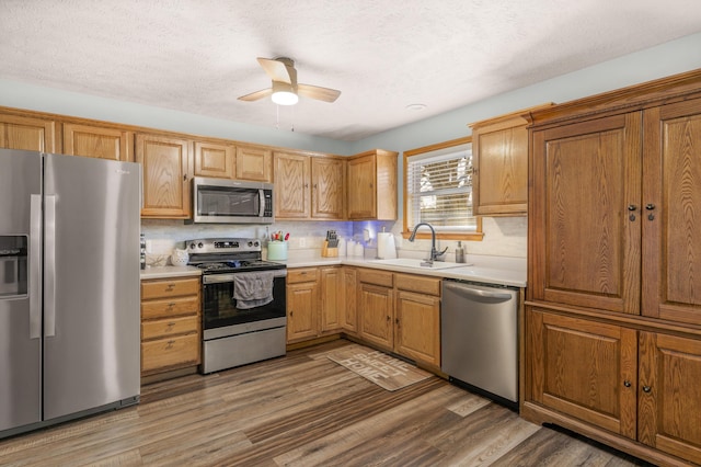 kitchen featuring a sink, wood finished floors, appliances with stainless steel finishes, light countertops, and ceiling fan