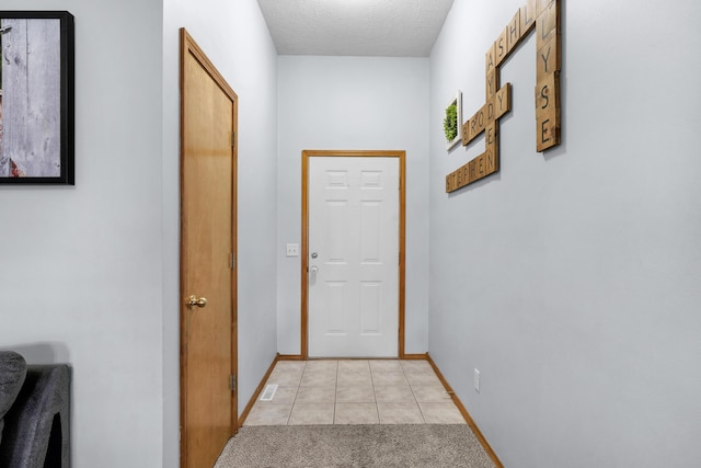 hall featuring a textured ceiling, light tile patterned floors, baseboards, and light carpet