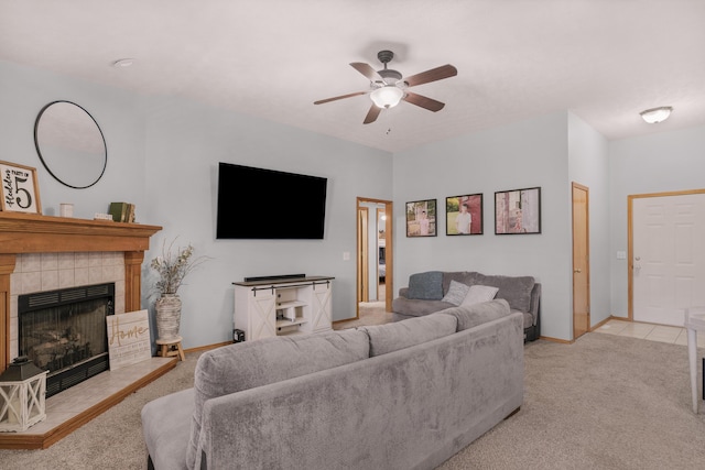 living room with a tiled fireplace, light colored carpet, baseboards, and a ceiling fan