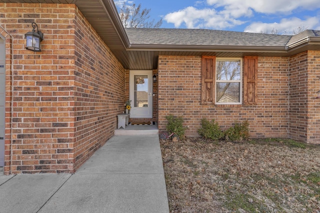 view of exterior entry with brick siding and a shingled roof