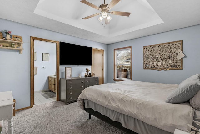 carpeted bedroom featuring connected bathroom, baseboards, tile patterned floors, a raised ceiling, and a ceiling fan