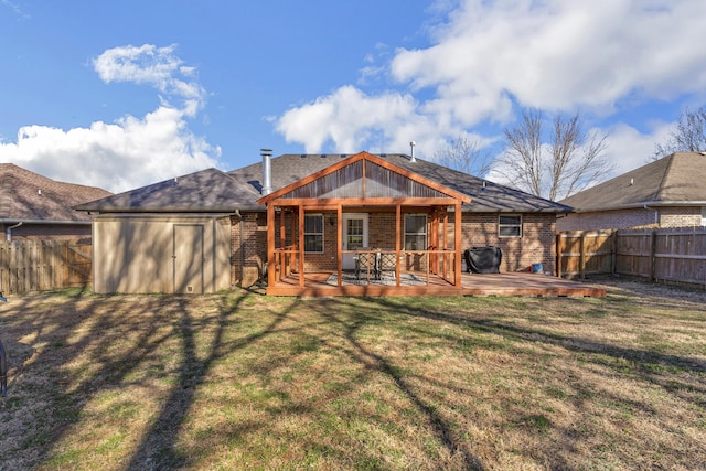 back of property featuring a yard, a deck, brick siding, and a fenced backyard