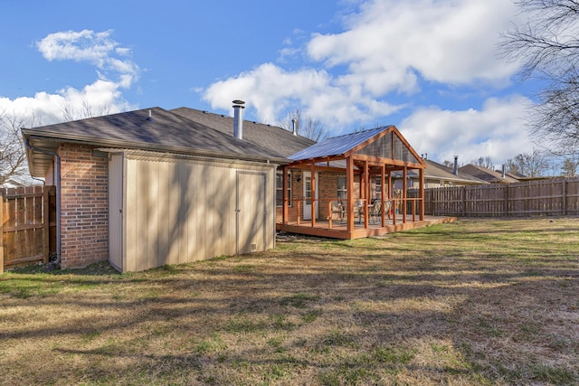 back of house with brick siding, roof with shingles, a lawn, a deck, and a fenced backyard