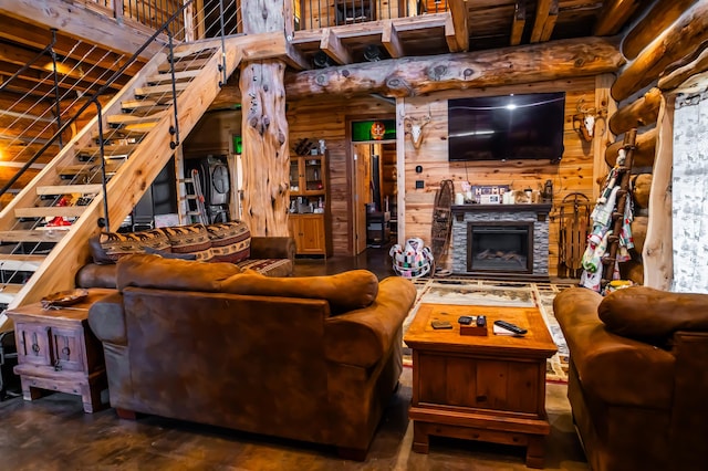 living area with a stone fireplace, stairway, log walls, and wooden walls