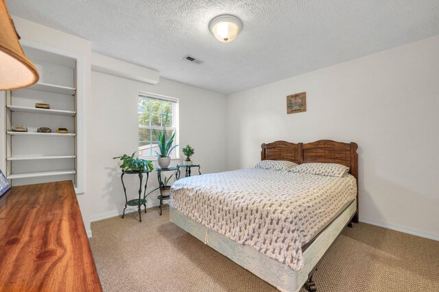 carpeted bedroom featuring baseboards, visible vents, and a textured ceiling