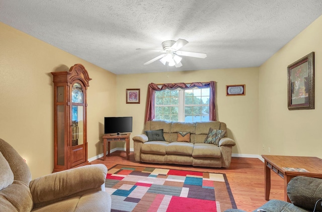 living area featuring baseboards, a textured ceiling, wood finished floors, and a ceiling fan