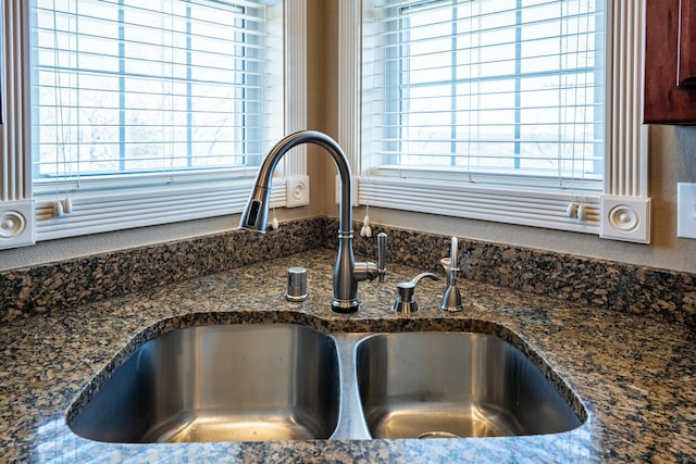 room details with dark stone counters, a textured wall, and a sink