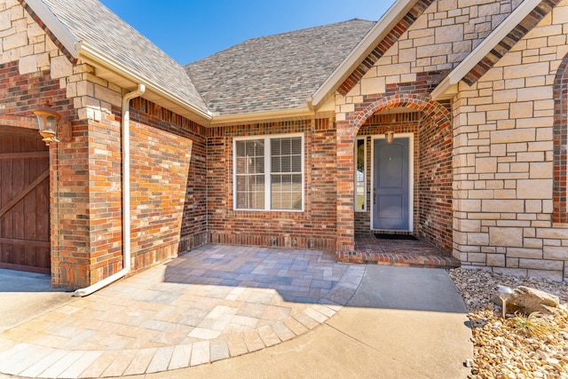 property entrance featuring brick siding, an attached garage, and a shingled roof