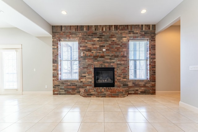 unfurnished living room featuring tile patterned flooring, a brick fireplace, a healthy amount of sunlight, and baseboards