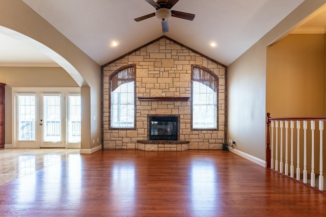 unfurnished living room featuring wood finished floors, baseboards, lofted ceiling, ceiling fan, and a stone fireplace