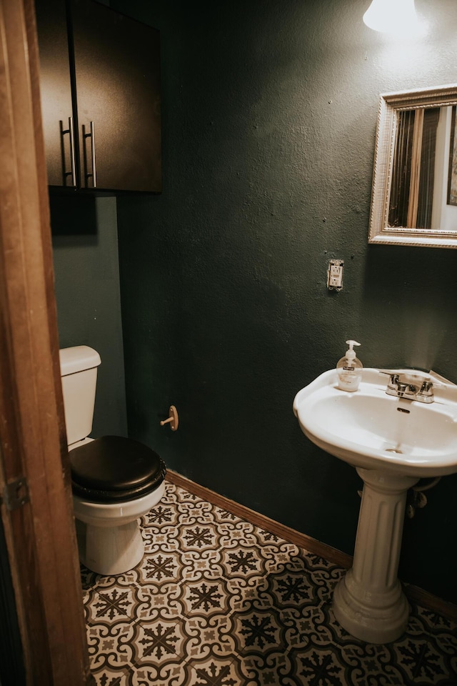 bathroom with tile patterned flooring, toilet, a textured wall, and baseboards