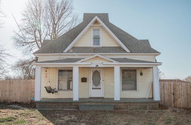 bungalow featuring a porch, roof with shingles, and fence