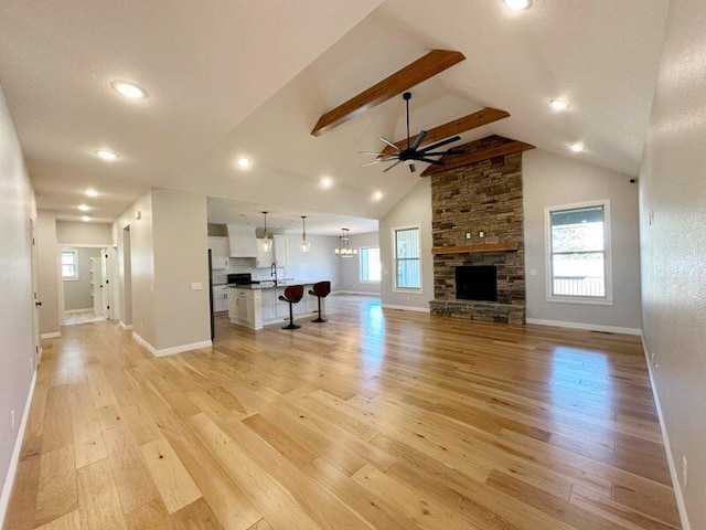 unfurnished living room with baseboards, light wood-type flooring, a stone fireplace, ceiling fan with notable chandelier, and a sink