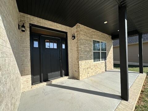 view of exterior entry featuring brick siding and covered porch