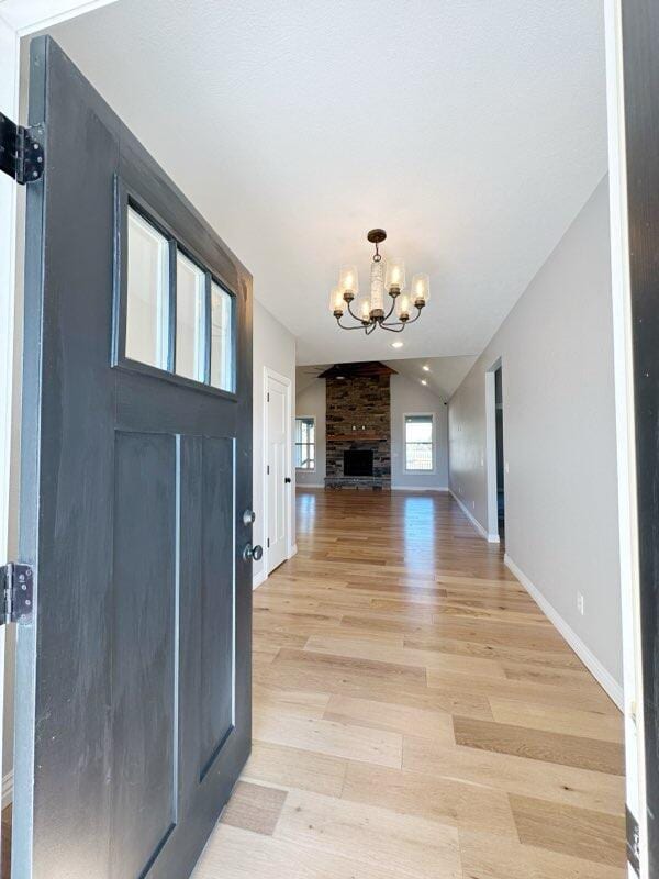 foyer entrance with a notable chandelier, light wood-style flooring, baseboards, and lofted ceiling