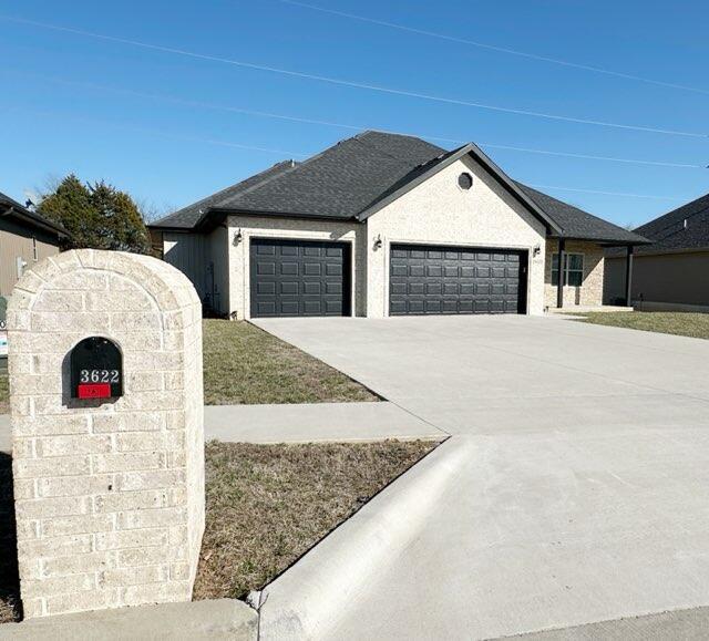 single story home with concrete driveway, a garage, and a shingled roof