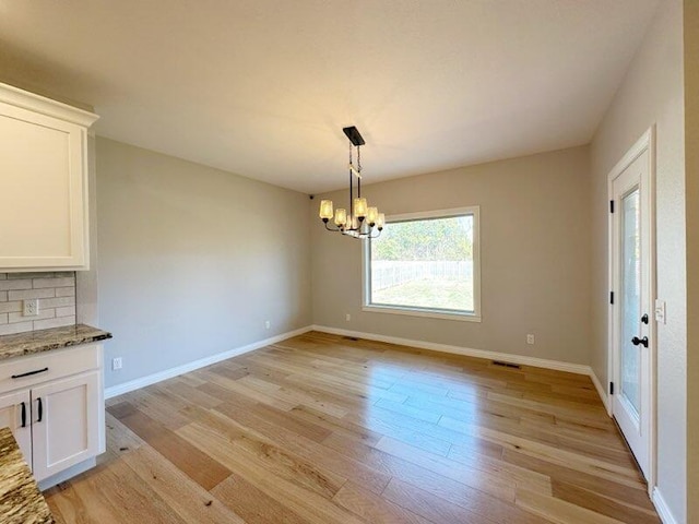 unfurnished dining area featuring light wood-type flooring, baseboards, a notable chandelier, and visible vents