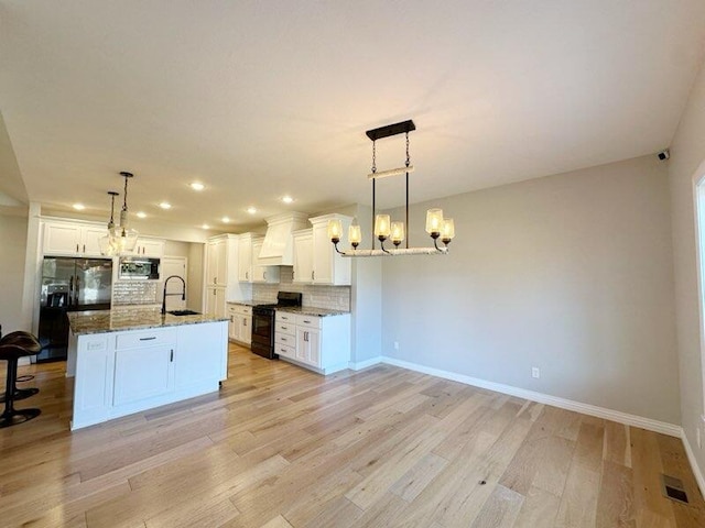 kitchen with a sink, black appliances, custom range hood, backsplash, and a chandelier