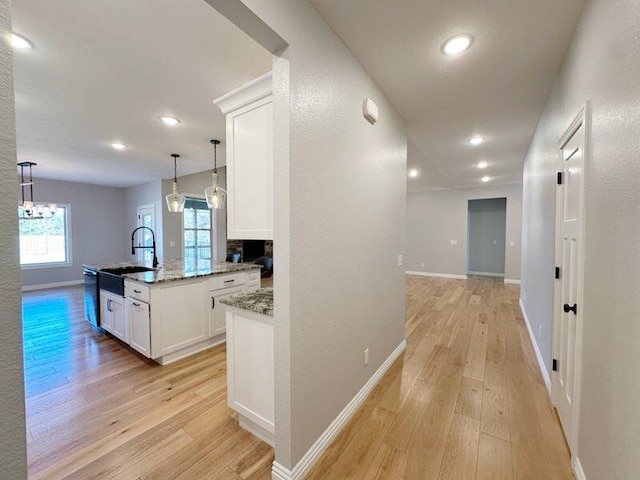 hall featuring a sink, baseboards, an inviting chandelier, and light wood finished floors