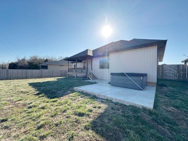 rear view of property featuring a yard, a patio, a fenced backyard, and a hot tub