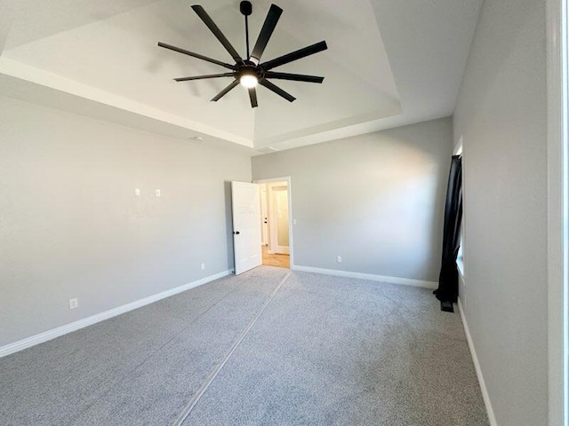 carpeted empty room featuring a tray ceiling, a ceiling fan, and baseboards