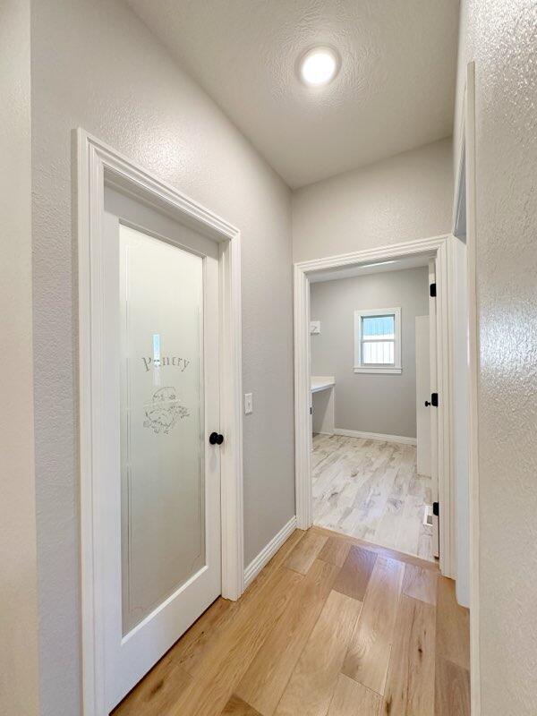 corridor with baseboards, a textured ceiling, light wood-style flooring, and a textured wall