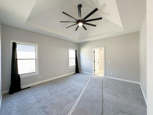 carpeted empty room featuring a tray ceiling, baseboards, and a ceiling fan