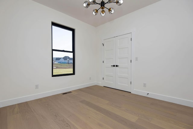 empty room with an inviting chandelier, light wood-style floors, visible vents, and baseboards