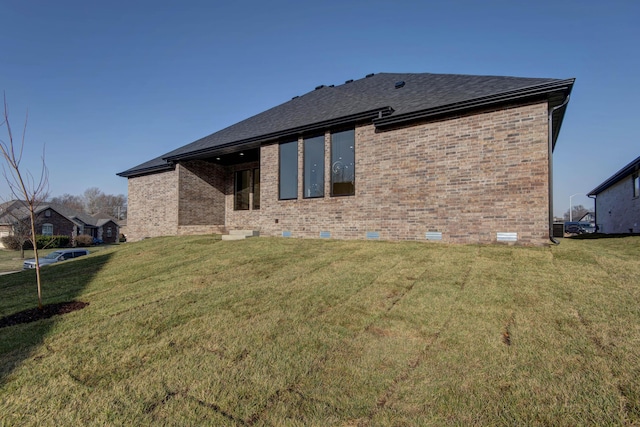 back of property featuring a lawn, brick siding, roof with shingles, and crawl space