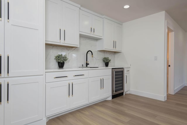 bar featuring light wood-style flooring, beverage cooler, a sink, tasteful backsplash, and baseboards