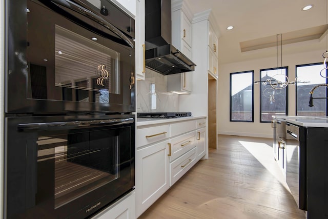 kitchen with light wood-type flooring, dobule oven black, wall chimney range hood, backsplash, and light countertops